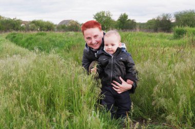 Woman with a small son among tall grass. Woman with a small child walk along the meadows. Woman with short red hair. 