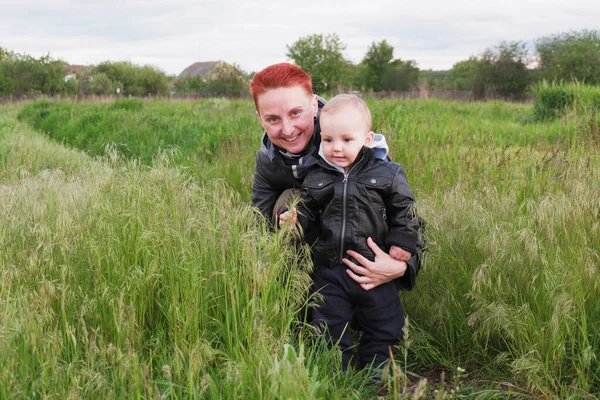 Woman with a small son among tall grass. Woman with a small child walk along the meadows. Woman with short red hair. 