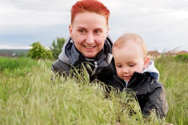 Woman with a small son among tall grass. Woman with a small child walk along the meadows. Woman with short red hair. 