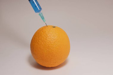 Injection of toxin into an orange. Laboratory tests. Injecting blue liquid into an orange fruit. Syringe with blue liquid on the white background.