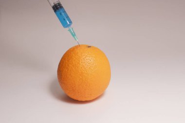 Injection of toxin into an orange. Laboratory tests. Injecting blue liquid into an orange fruit. Syringe with blue liquid on the white background.