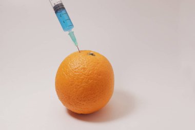 Injection of toxin into an orange. Laboratory tests. Injecting blue liquid into an orange fruit. Syringe with blue liquid on the white background.
