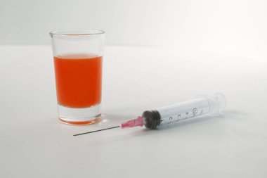 Syringe and glass on a white background. Syringe with orange liquid on the white background. 