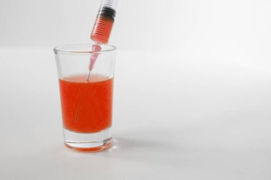 Syringe and glass on a white background. Syringe with orange liquid on the white background. 