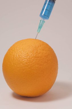 Injecting blue liquid into an orange fruit. Syringe with blue liquid on the white background.