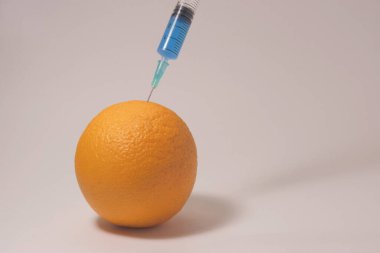 Injecting blue liquid into an orange fruit. Syringe with blue liquid on the white background.