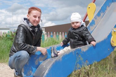 Kid in the playground. A little boy rides on the children's slide. Mom plays with the baby in the playground