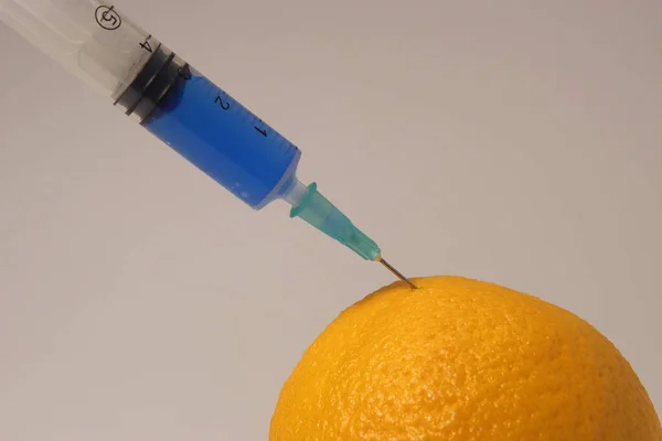 Injection of toxin into an orange. Laboratory tests. Injecting blue liquid into an orange fruit. Syringe with blue liquid on the white background.