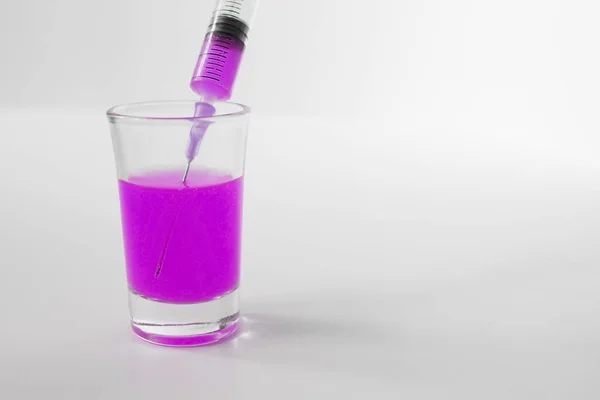 Purple injection. A glass with purple liquid and an empty syringe. Syringe on a white background. 