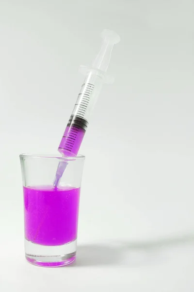 Purple injection. A glass with purple liquid and an empty syringe. Syringe on a white background. 
