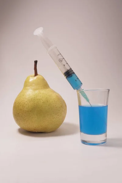 Yellow pear, syringe and glass on a white background. Injection of blue fluid.