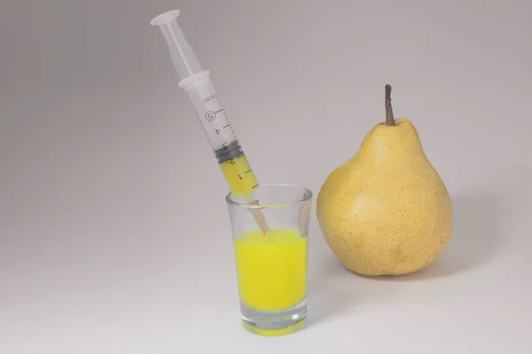 Yellow pear, syringe and glass on a white background. Injection of yellow fluid.