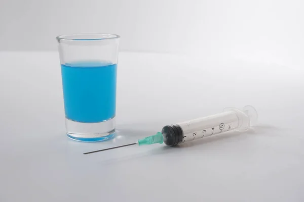 Syringe with blue liquid on the white background. Glass cup with blue liquid on the white background.