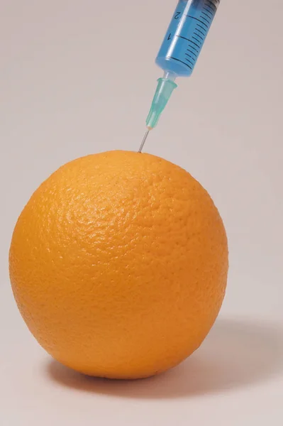 Injecting blue liquid into an orange fruit. Syringe with blue liquid on the white background.