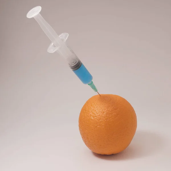 Injecting blue liquid into an orange fruit. Syringe with blue liquid on the white background.
