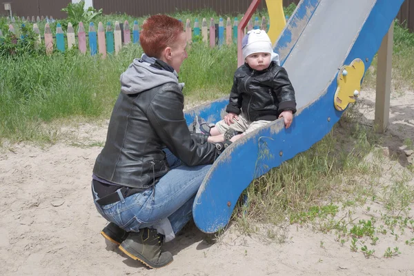 Mom plays with the baby in the playground. Kid in the playground. A little boy rides on the children's slide. 