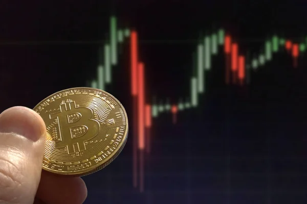 Hand holding golden Bitcoin with blurred financial stock market graph chart of stock market investment trading screen background