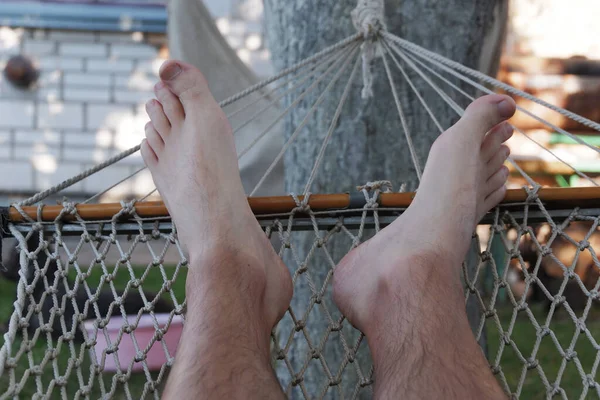 A man lies in a hammock. Male legs close-up. Recreation in nature. Relax Summer vacations. Mesh hammock.