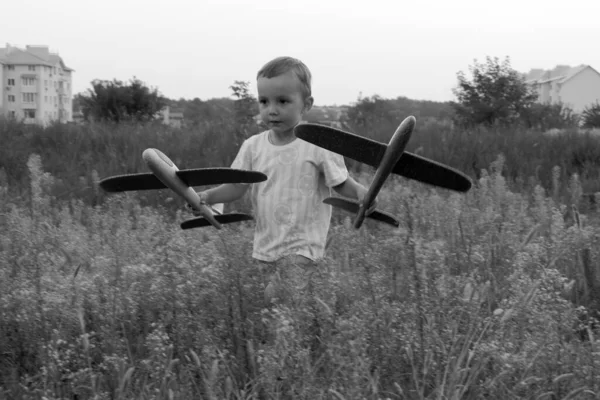Monochrome photo. Little boy launches toy airplanes. Young aviator. The boy dreams of becoming an airplane pilot.