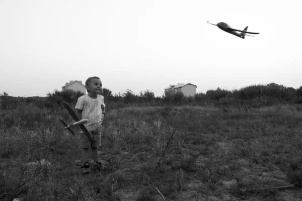 Monochrome photo. Little boy launches toy airplanes. Young aviator. The boy dreams of becoming an airplane pilot.