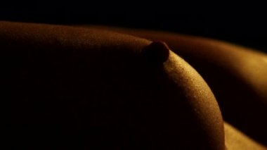 Light and shadow on the female breast. A nude young woman with beautiful breasts lies on her back. In the twilight. Part of the body close-up.