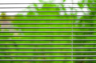 Pencerenin dışındaki bulanık yaz manzaralı açık panjurlar ya da siyah panjurlar.