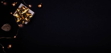 Noel hediyesi. Altın yay, altın toplar ve parlak ışık çelenkleriyle dolu beyaz bir hediye. Karanlık arka planda tebrik kartı için. Metin için alanı olan Xmas arkaplanı