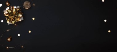Noel hediyesi. Altın yay, altın toplar ve parlak ışık çelenkleriyle dolu beyaz bir hediye. Karanlık arka planda tebrik kartı için. Metin için alanı olan Xmas arkaplanı