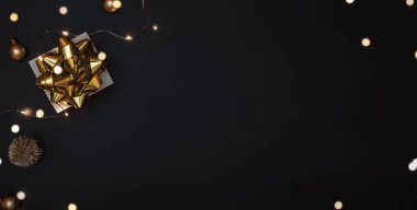 Noel hediyesi. Altın yay, altın toplar ve parlak ışık çelenkleriyle dolu beyaz bir hediye. Karanlık arka planda tebrik kartı için. Metin için alanı olan Xmas arkaplanı