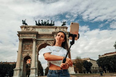 Seyahat blogcusu Milan Italya. Milan Piazza del Duomo 'da akıllı telefonu olan fotoğrafçı kız. Avrupa 'da Milano şehrinde boyama evi. Telefonunu açık havada kullanan bir turist.