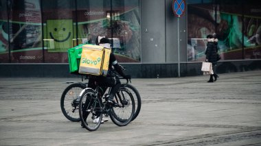 KATOWICE. POLAND - 26 Mart 2021: hızlı restoran teslimatı için bisikletli ya da motosikletli adam. Paket servisi için yemek paketi. Glovo kuryesi scooter 'da yemek getiriyor.