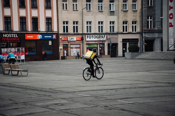 KATOWICE. POLAND - 26 Mart 2021: hızlı restoran teslimatı için bisikletli ya da motosikletli adam. Paket servisi için yemek paketi. Glovo kuryesi scooter 'da yemek getiriyor.