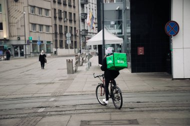 KATOWICE. POLAND - 26 Mart 2021: teslimat servisi için yemek çantası. Hızlı restoran teslimatı için bisikletli ya da motosikletli adam. Uber ekspres gıda dağıtım servisi yiyor