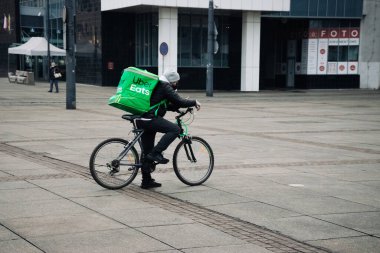 KATOWICE. POLAND - 26 Mart 2021: hızlı restoran teslimatı için bisikletli ya da motosikletli adam. Paket servisi için yemek paketi. Uber teslimatı yapan motosiklet yiyecek ekspres servisi yiyor