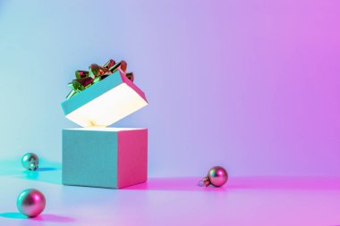Noel kompozisyonu neon. Parlak ışıklarla dolu Xmas hediye kutusunu aç, en az ağaçla. Neon soyut gradyan arkaplan üzerinde bayram süsleme takısı topu. Yeni yıl afişi