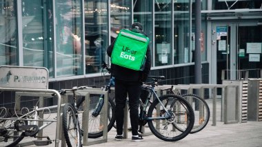 KATOWICE. POLAND - 26 Mart 2021: hızlı restoran teslimatı için bisikletli ya da motosikletli adam. Paket servisi için yemek paketi. Uber teslimatı yapan motosiklet yiyecek ekspres servisi yiyor