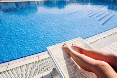 Yaz eğlencesi. Bikini mayo giymiş, güneş gözlüklü, tatil köyünde oturan genç ve seksi bir kız. Lüks otel mavi su havuzunda rahatla. Yüzme suyu, eğlenme ve seyahatin tadını çıkarma.