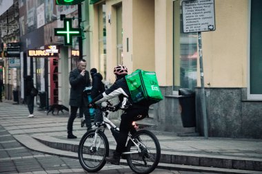 KATOWICE. POLAND - 26 Mart 2021: hızlı restoran teslimatı için bisikletli ya da motosikletli adam. Paket servisi için yemek paketi. Uber yemek dağıtırken mobiletle kurye yiyor.
