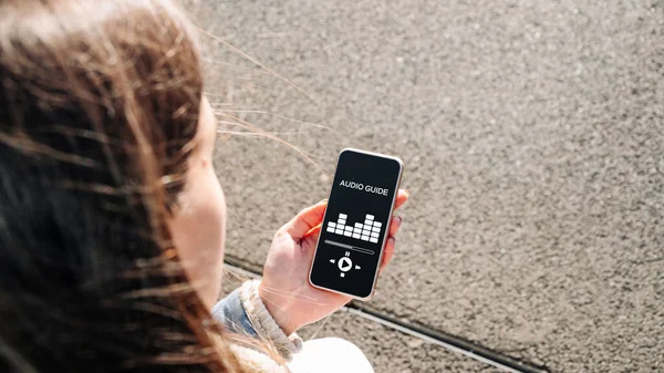 Dijital mobil akıllı telefondan ses turu uygulaması. Telefonu dinleyen genç ve mutlu bir bayan öğrenci. Eş zamanlı çeviri aygıtları