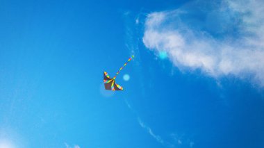 Uçurtma arka planı. Renkli, yüksek uçan oyuncak. Hava uçurtması mavi rüzgar gökyüzünde uçar. Yaz bulutlarında gökkuşağı uçurtması. Şenlik, mutluluk, başarı geçmişi