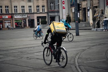 KATOWICE. POLAND - 26 Mart 2021: hızlı restoran teslimatı için bisikletli ya da motosikletli adam. Paket servisi için yemek paketi. Glovo kuryesi scooter 'da yemek getiriyor.