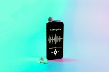 Dijital mobil akıllı telefon ekranında müzik kulaklığı ve neon arka planda ses rehberi uygulaması. Gezintilerin ses rehberini dinlemek için aygıtlar