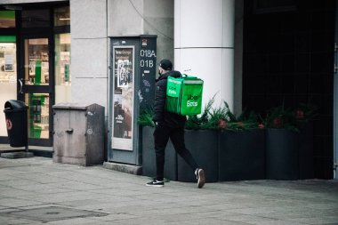 KATOWICE. POLAND - 26 Mart 2021: hızlı restoran teslimatı için bisikletli ya da motosikletli adam. Paket servisi için yemek paketi. Uber yemek dağıtırken mobiletle kurye yiyor.