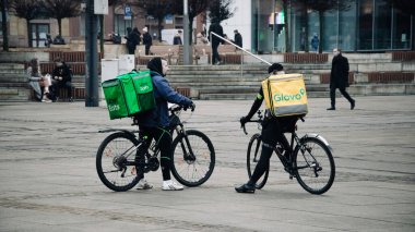 KATOWICE. POLAND - 26 Mart 2021: hızlı restoran teslimatı için bisikletli ya da motosikletli adam. Paket servisi için yemek paketi. Glovo kuryesi scooter 'da yemek getiriyor.