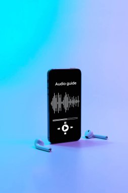 Dijital mobil akıllı telefon ekranında müzik kulaklığı ve neon arka planda ses rehberi uygulaması. Gezintilerin ses rehberini dinlemek için aygıtlar