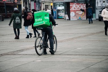 KATOWICE. POLAND - 26 Mart 2021: hızlı restoran teslimatı için bisikletli ya da motosikletli adam. Paket servisi için yemek paketi. Uber teslimatı yapan motosiklet yiyecek ekspres servisi yiyor