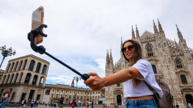 Gezginler Milan adasını etkiliyor. Avrupa 'da boyama evi Milano' da. Piazza del Duomo, Katedral Meydanı 'nda akıllı telefonlu fotoğrafçı kız. Seyahat ve serbest çalışma, modern yaşam tarzı.