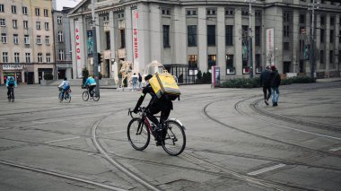 KATOWICE. POLAND - 26 Mart 2021: hızlı restoran teslimatı için bisikletli ya da motosikletli adam. Paket servisi için yemek paketi. Glovo kuryesi scooter 'da yemek getiriyor.