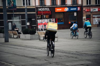 KATOWICE. POLAND - 26 Mart 2021: hızlı restoran teslimatı için bisikletli ya da motosikletli adam. Paket servisi için yemek paketi. Glovo kuryesi scooter 'da yemek getiriyor.