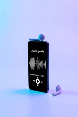 Dijital mobil akıllı telefon ekranında müzik kulaklıkları ve neon arka planda sesli gezinti uygulaması. Ses rehberini dinliyorum. Eğitim ve eğlence kavramı